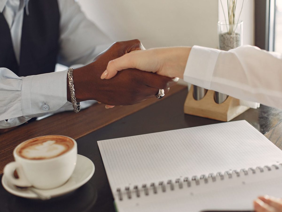 Two people shaking hands across a table with a notebook