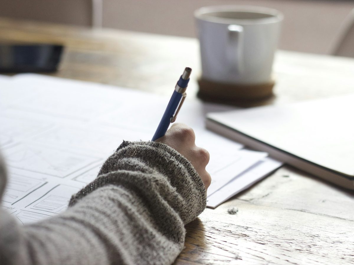 A hand writing notes in a notebook on a wooden desk