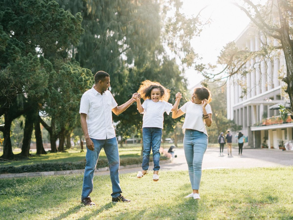 A father and mother swinging their child between them outdoors